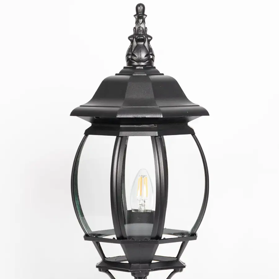 Closeup of decorative black pillar light with curved glass panels and LED bulb showcasing elegant outdoor lighting.
