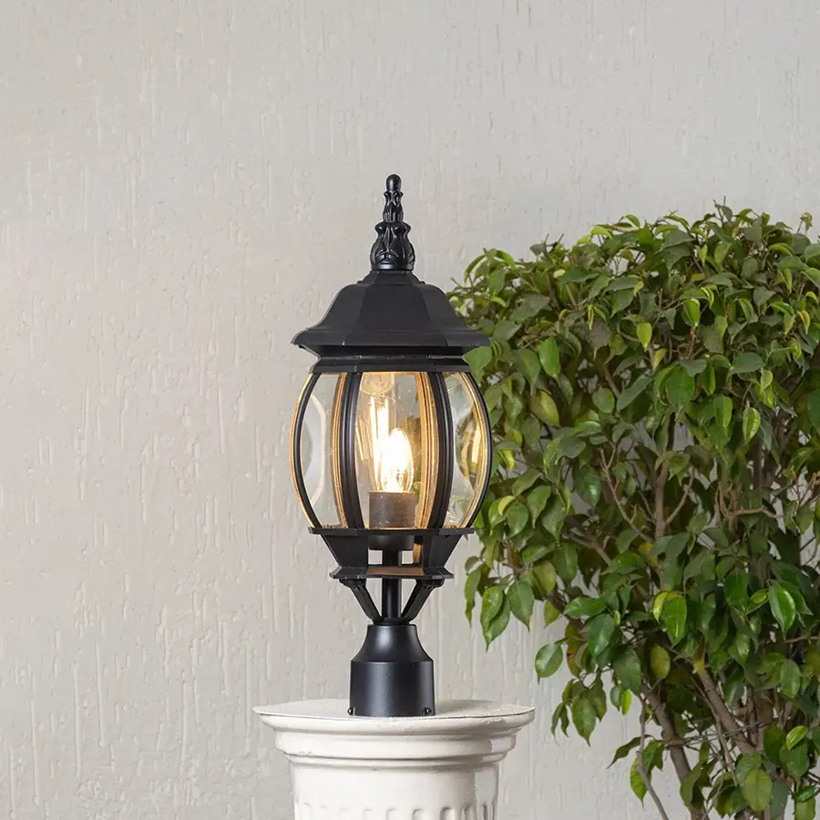 Black metal outdoor pillar lamp glowing with curved glass shade placed on stone pillar ideal for garden and patio decor.