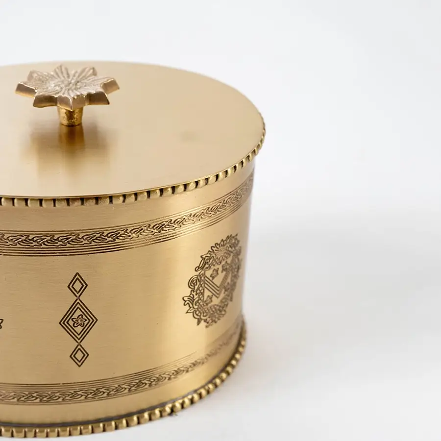 Open gold metal round storage jar with engraved details and lid placed beside it on plain white background.