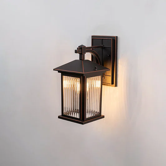 Bronze metal outdoor wall light on white background with ribbed glass shade illuminating a warm light for patio decor.