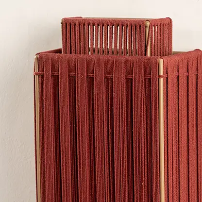 Closeup of red jute wall lamp reveals fine woven details and expert craftsmanship that exude warmth and natural sophistication.