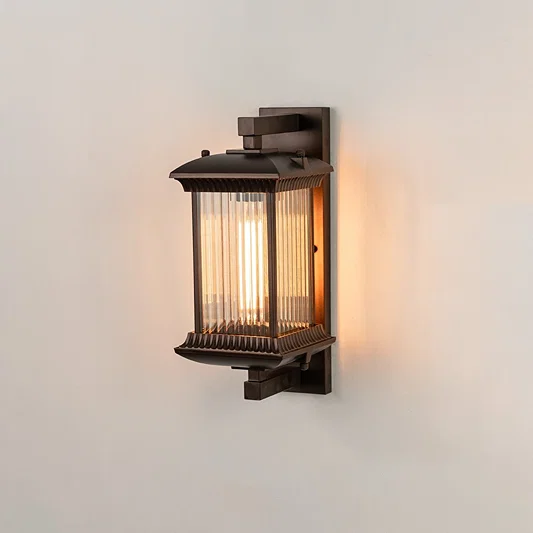 Antique bronze metal outdoor wall light on white background with ribbed glass shade illuminating warm patio decor.