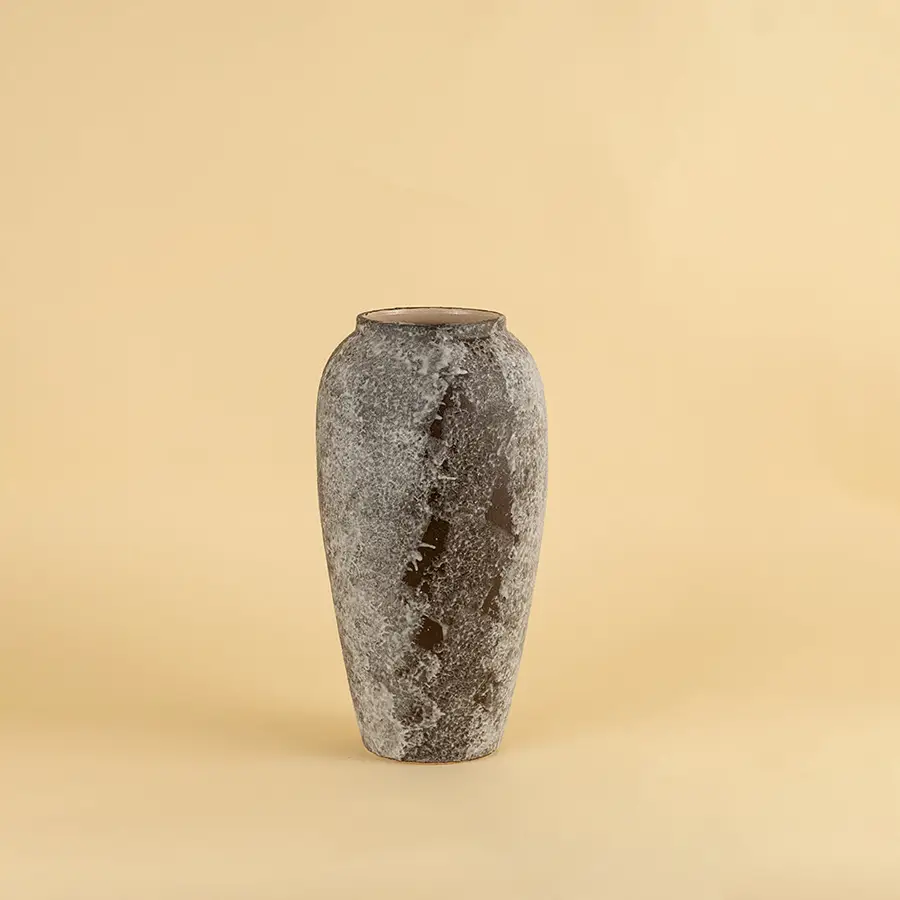 Grey textured ceramic vase with rough stone finish placed on beige surface against warm background showcasing rustic modern home decor styling.