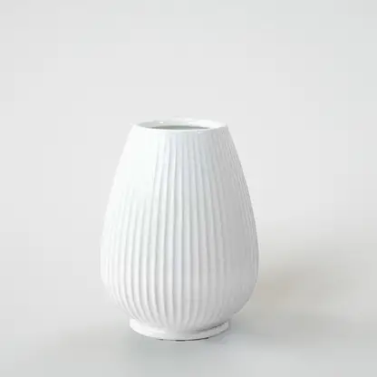 White ribbed ceramic decorative vase with curved silhouette for shelf styling and contemporary home decor displays.