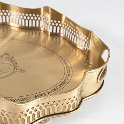 A closeup view of the gold serving tray showing its intricate engraved center scalloped border and fine metal texture with detailed craftsmanship visible.