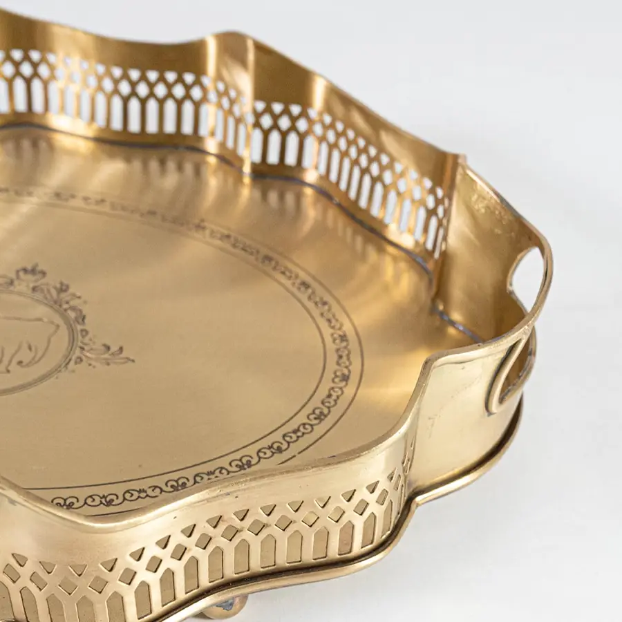 A closeup view of the gold serving tray showing its intricate engraved center scalloped border and fine metal texture with detailed craftsmanship visible.