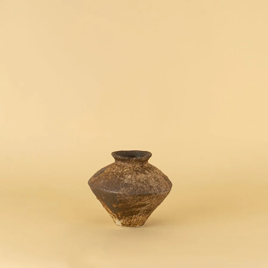 Traditional ceramic pot with earthy brown tone and aged texture placed on beige surface against warm background highlighting antique inspired home decor appeal.