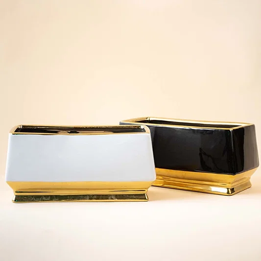 A modern pair of rectangular ceramic vases in glossy black and matte white finished with elegant gold bases displayed together on a wooden surface creating a balanced decorative look that highlights their contrasting colors and contemporary style.