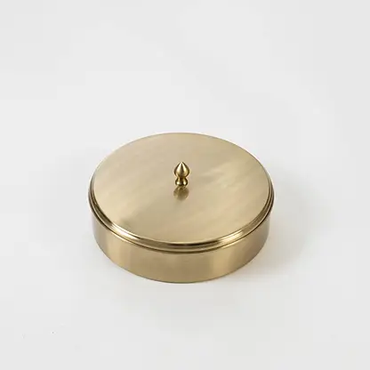 Round brass spice box packed in a black branded gift box with lid partially open shown on clean white background.