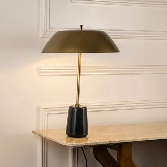 Table lamp with gold metal base and wide shade perfect for bedroom or living room table decor styling on clean white background.