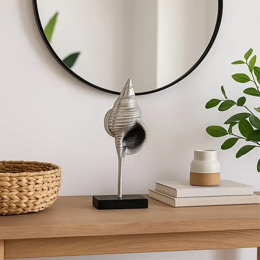Silver metal conch sculpture on a black stand styled in a modern room adding coastal artistic decor to shelves consoles and contemporary interiors.