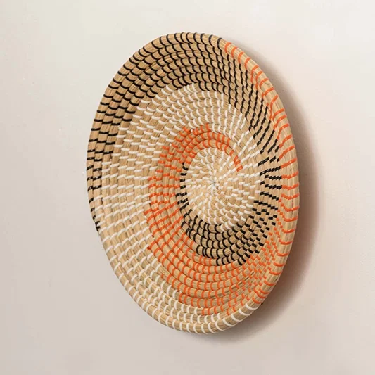 Side angle view of handwoven spiral wall plate in natural beige with orange and black accents.