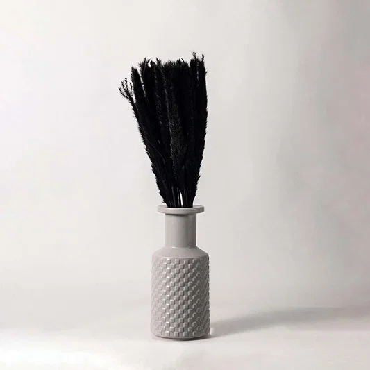 A decorative vase with a textured pattern holding tall black dried stems placed against a clean white background showing a minimal and modern home decor accent.
