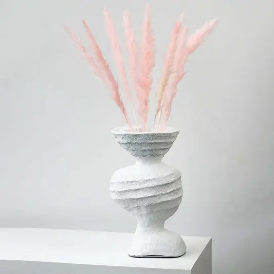 Light pink pampas grass stems styled in textured white ceramic vase elegant boho home decor on white backdrop