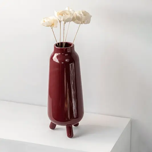 Elegant burgundy vase placed on a minimalist white shelf highlighting its tall structure and deep red hue for contemporary home décor.