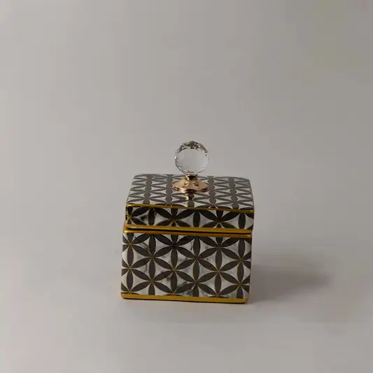 Decorative ceramic jar with gold geometric lattice pattern and crystal knob lid placed on white surface against neutral background showcasing luxury modern home decor styling.