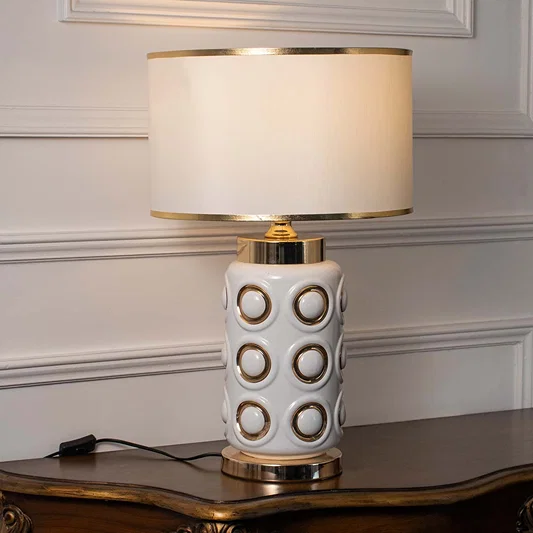White ceramic table lamp with geometric gold accents and fabric shade for modern luxury interior styling.