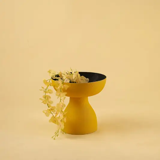 Vibrant yellow metal pedestal bowl with trailing plant for modern home decor and artistic tabletop centerpiece style.