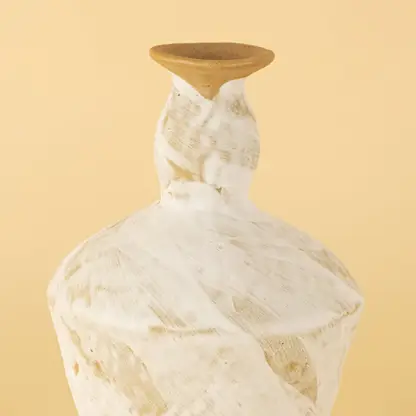 Closeup image of a handcrafted ceramic decorative vase featuring a whitewashed textured finish with natural earthy tones placed on a soft beige background highlighting artisanal surface details.