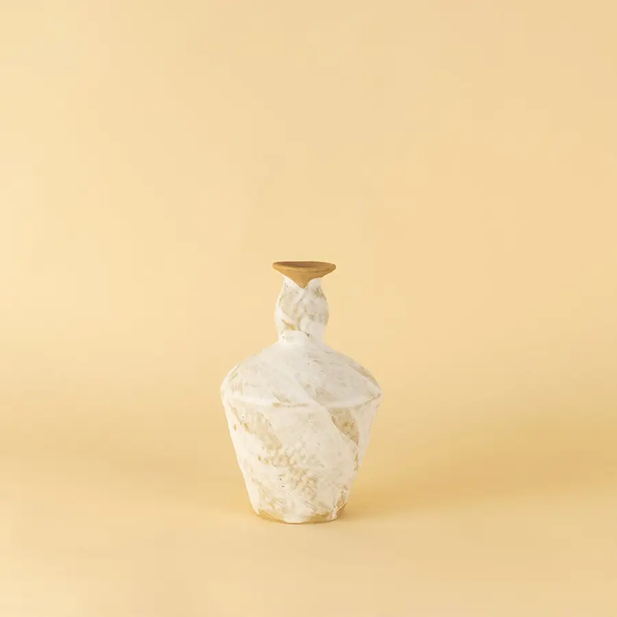 White ceramic vase with geometric textured design placed on beige surface against warm background showcasing modern sculptural home decor styling.