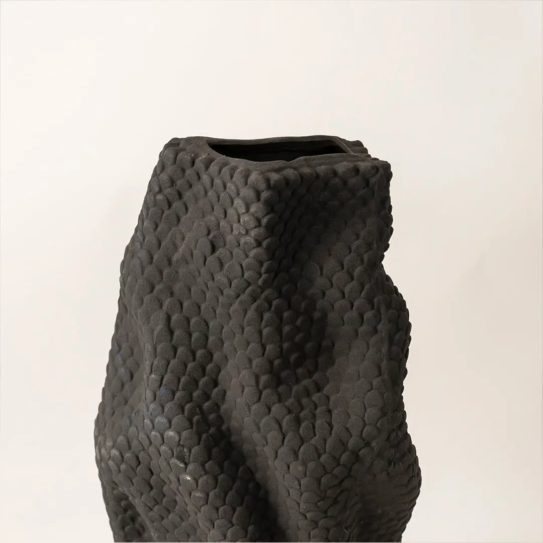 Closeup of black textured ceramic vase highlighting detailed gold dotted accent and handcrafted sculptural surface.