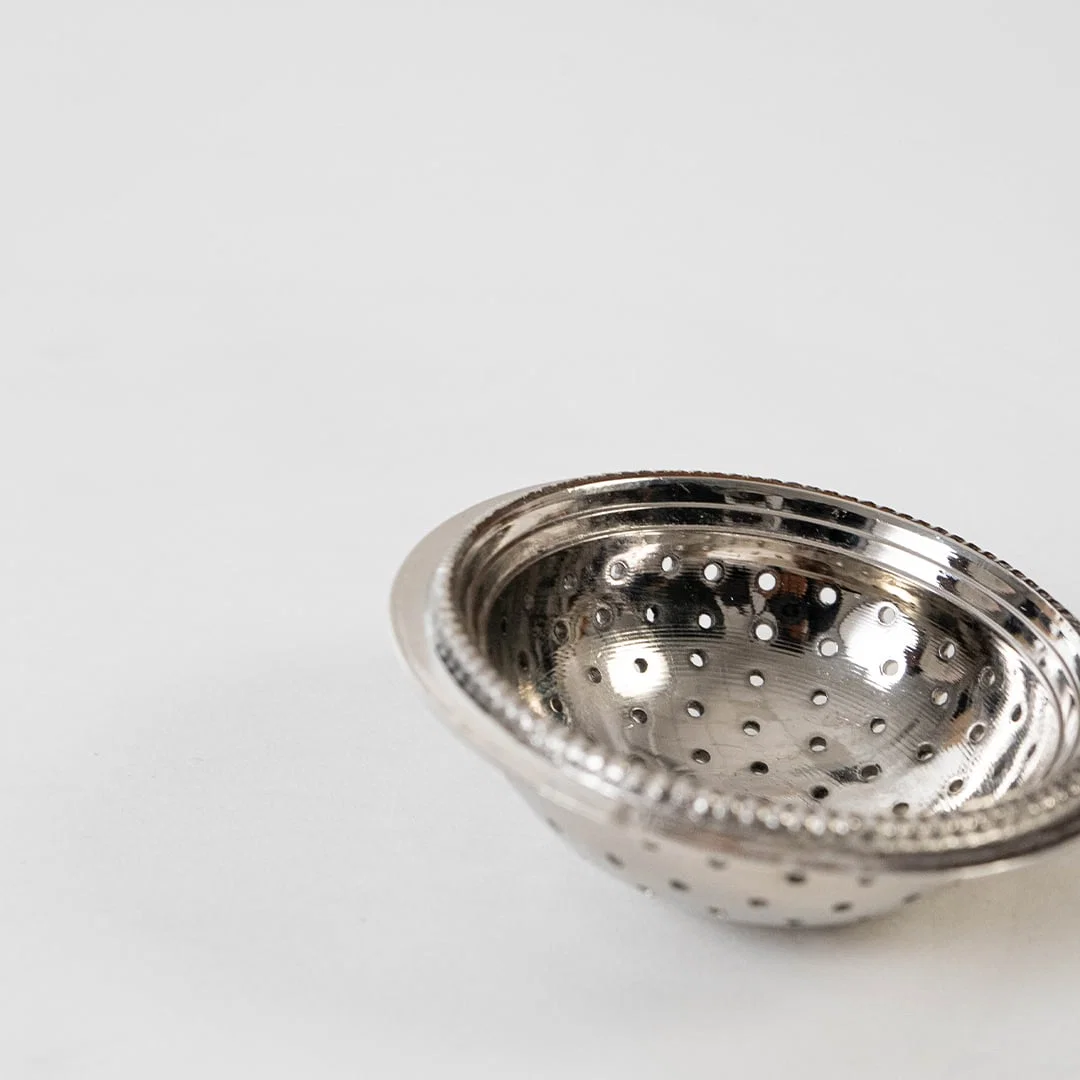 Detailed closeup view of the perforated holes and beaded rim design on the silver tea strainer head on a white background.