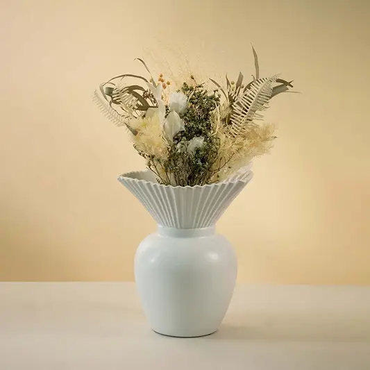 Modern white ceramic vase with pleated design styled with dried floral arrangement on wooden coffee table enhancing the elegant living room decor.