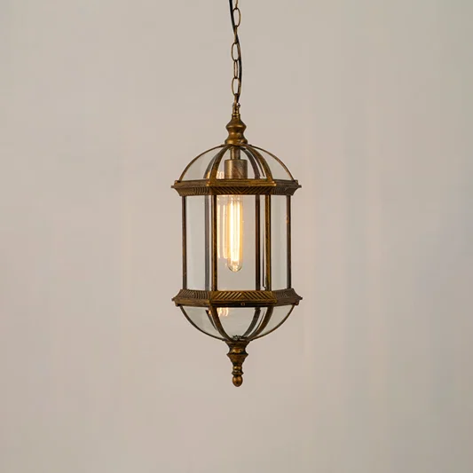 A bronze vintage style hanging lantern lit with a warm glow showcasing its elegant glass panels and dome top design suspended from a chain against a neutral wall backdrop.