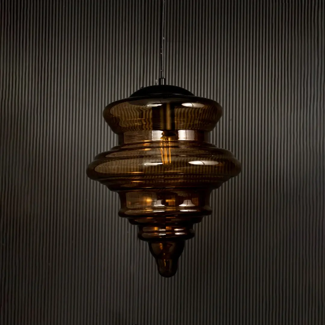 Amber glass pendant light displayed on dark background with lights off highlighting its glossy texture and sculptural design.
