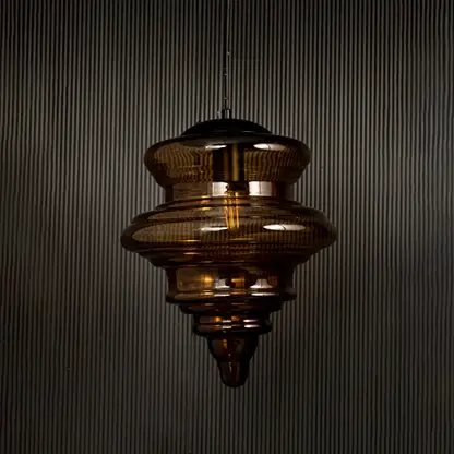 Amber glass pendant light displayed on dark background with lights off highlighting its glossy texture and sculptural design.