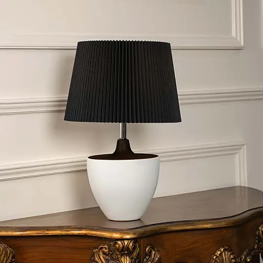 Black pleated shade table lamp with white ceramic base and dark metal stem for modern luxury interior styling.