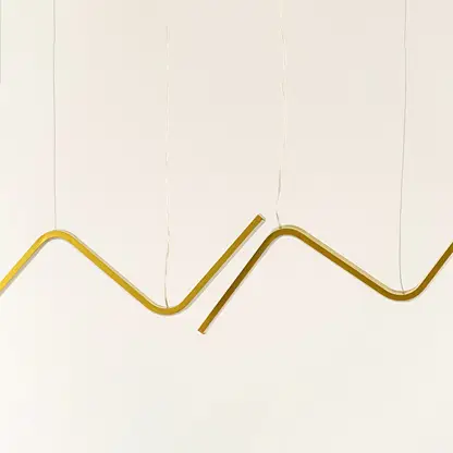 Gold sculptural chandelier featuring sweeping wave shaped LED bars suspended elegantly creating a warm dynamic decorative lighting accent in the modern room.