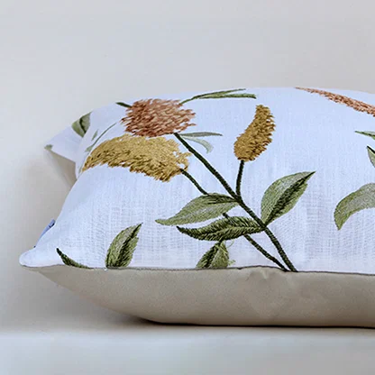 Closeup of the cushion showing detailed embroidered yellow and brown florals on soft white fabric.