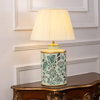 Table lamp on white background featuring teal floral ceramic base paired with a pleated fabric lampshade glowing softly.
