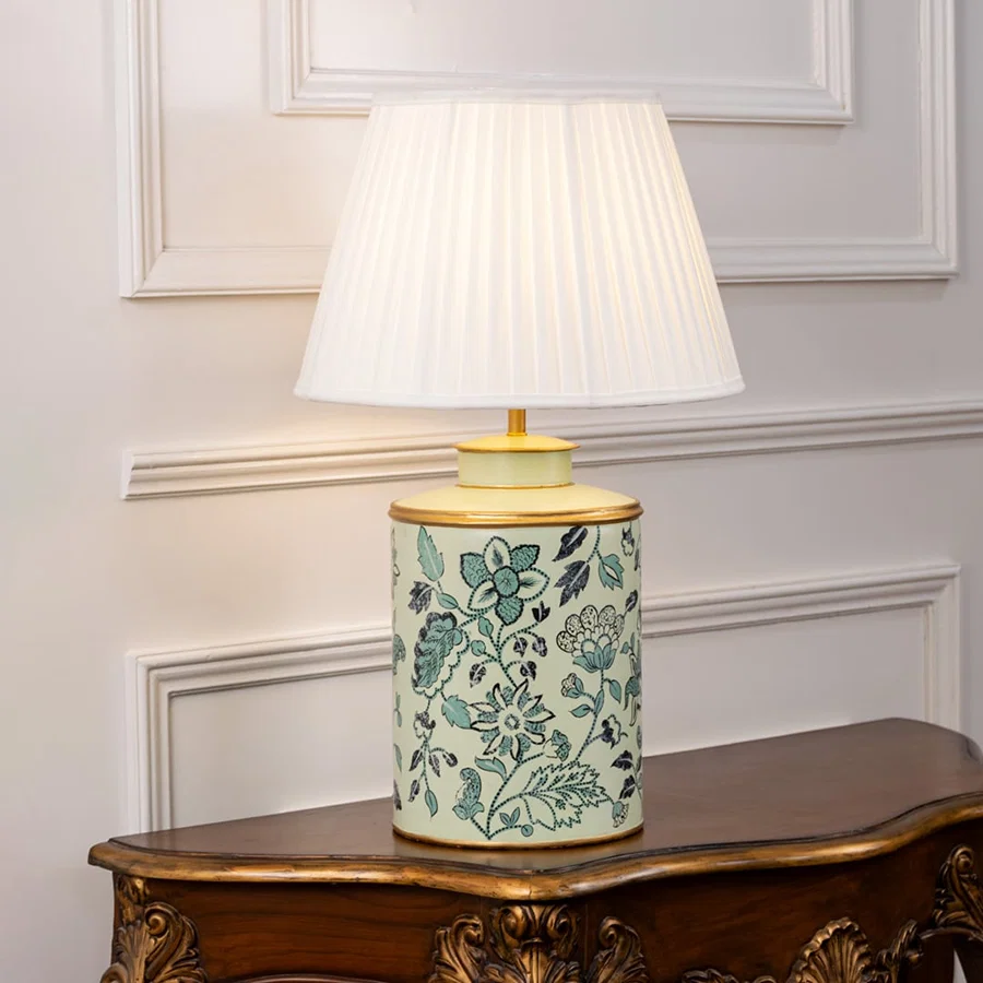 Table lamp showcasing a green floral ceramic base with a pleated lampshade placed against a white background.