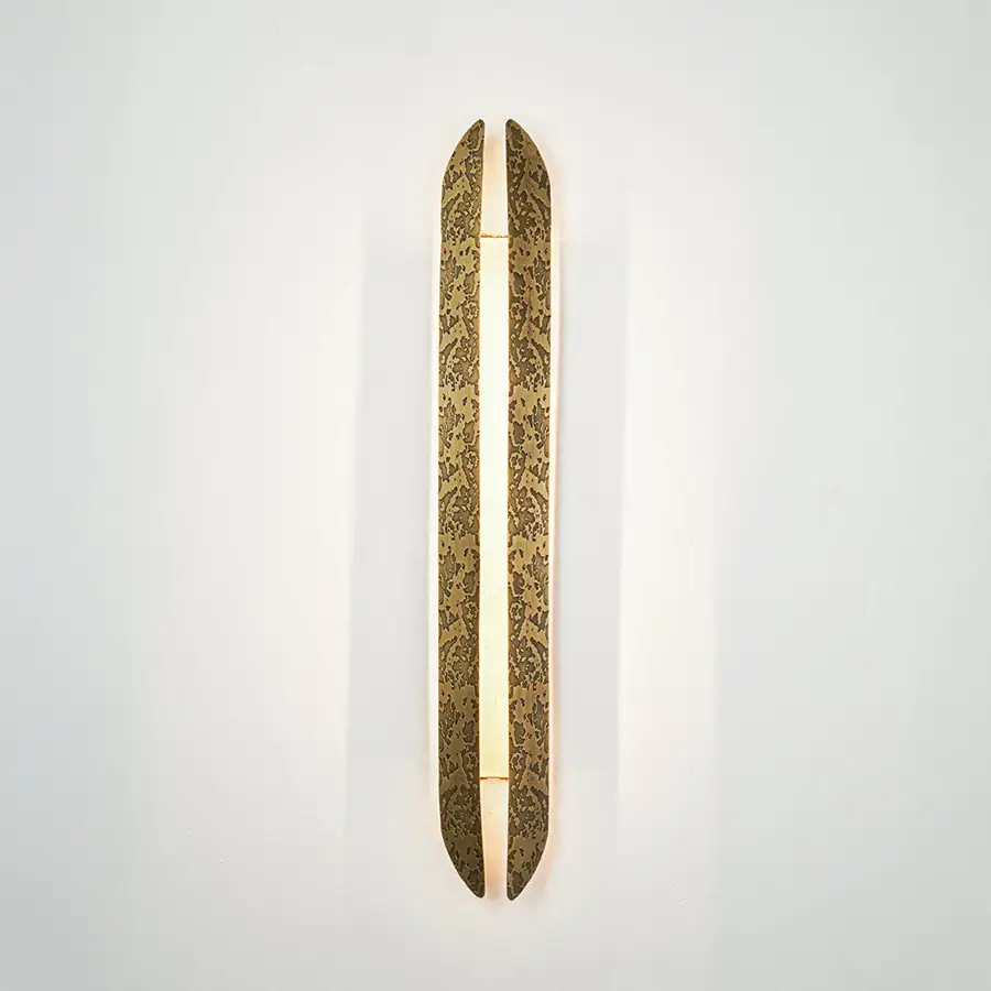 Gold wall light with elongated textured metal design mounted on neutral wall background ideal for modern luxury interior decor lighting.