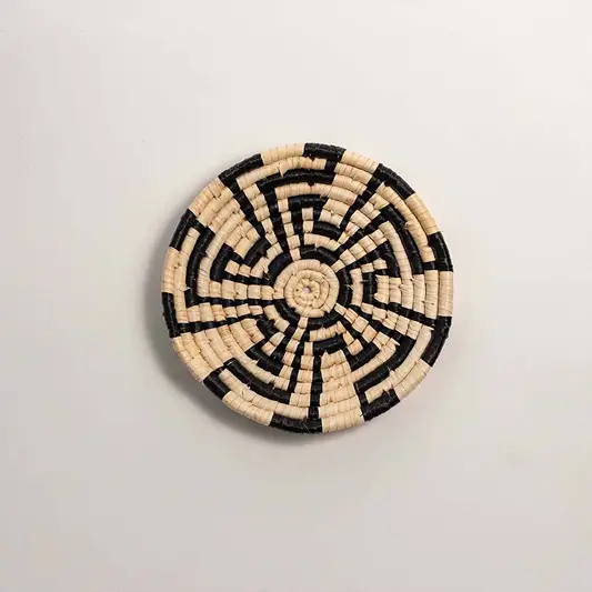 Round handcrafted black and cream seagrass wall basket with swirling abstract maze pattern on white background image.