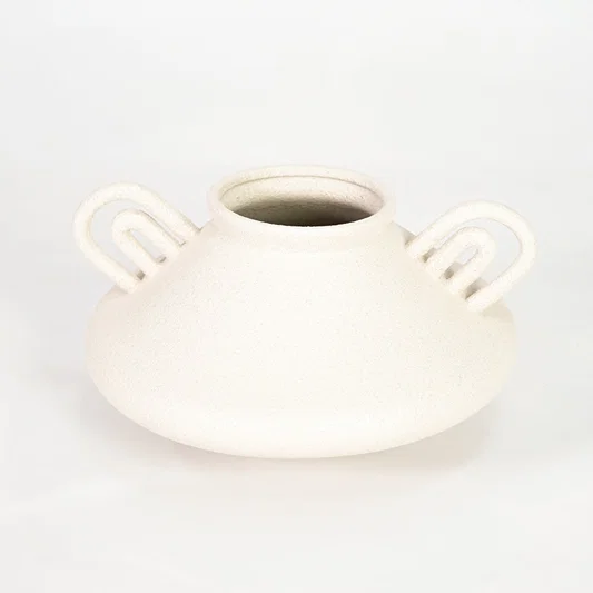 White ceramic vase with loop handles for modern shelf placement and elegant indoor home decor styling accent.