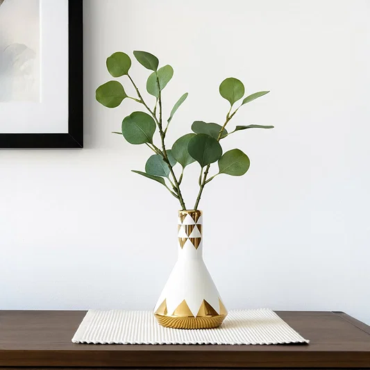White ceramic vase with green leafy stems styled on table creating fresh minimal look for modern interior Decor.