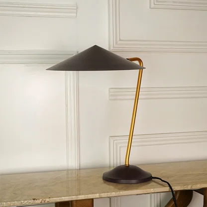 A modern table lamp with a dark brown conical shade and base, and a curved gold metal stem, shown on a marble tabletop against a white paneled wall.