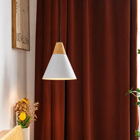 A modern pendant light with a white cone shade and natural wood accents hangs in front of dark rust-brown curtains in a styled interior setting.