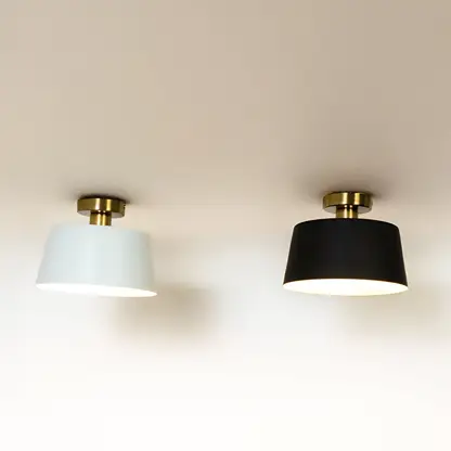 Black and white ceiling lights with gold fittings and drum shades glowing on white background for stylish modern home lighting.