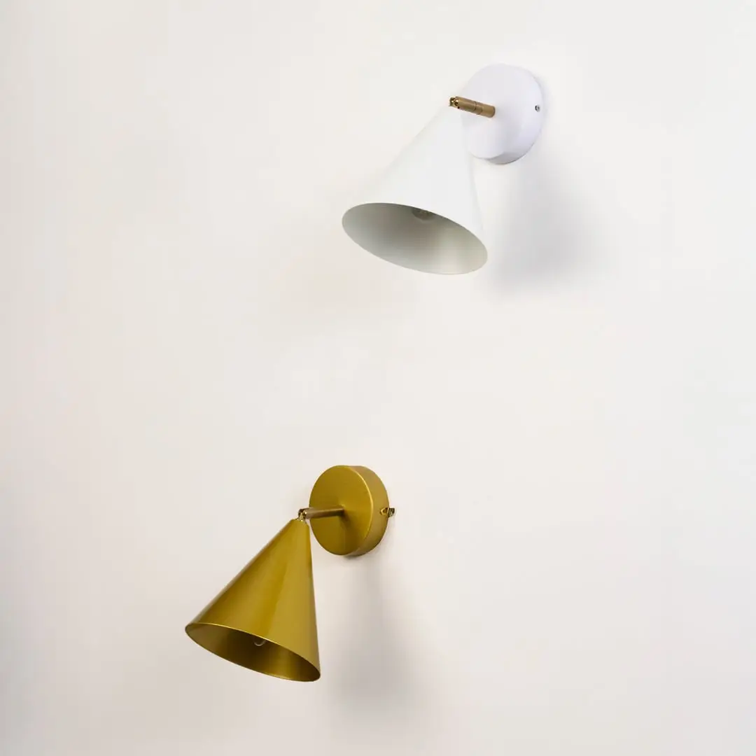 Two cone shaped wall sconces in white and gold mounted on a plain light wall with their shades angled downward.