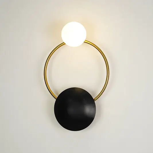 Contemporary gold brass hoop wall sconce featuring an illuminated frosted glass globe bulb on a white backdrop.