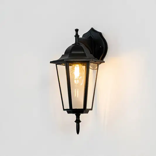 Black metal outdoor wall light on white background with clear glass shade for classic exterior decor.
