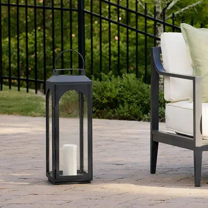 Modern black metal outdoor lantern with clear glass panels adding stylish ambient lighting beside comfortable patio seating.