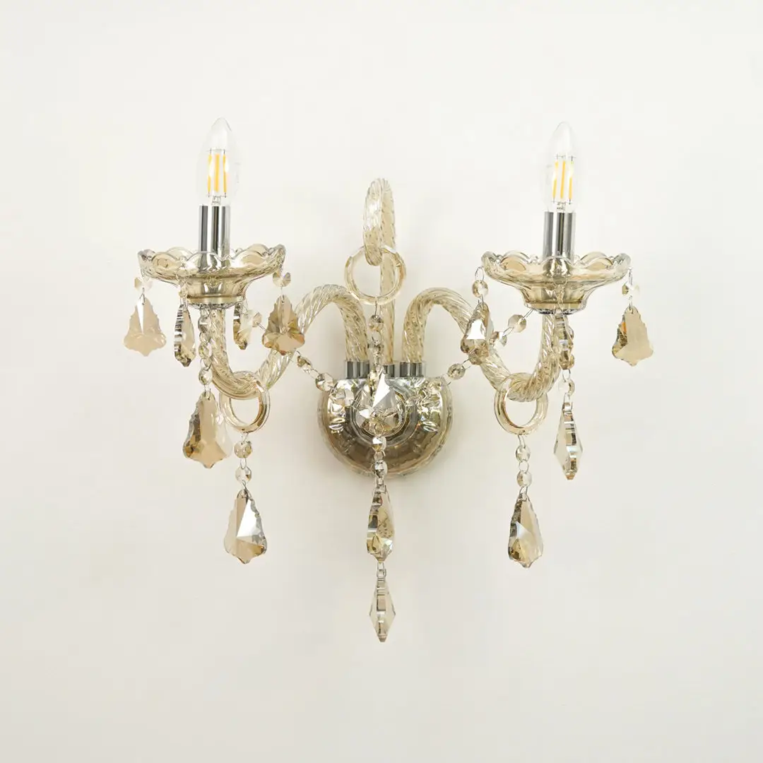 A double-arm wall sconce with a distressed silver metal finish, featuring clear glass candle-style bulbs and hanging faceted crystal drops against a plain white background.