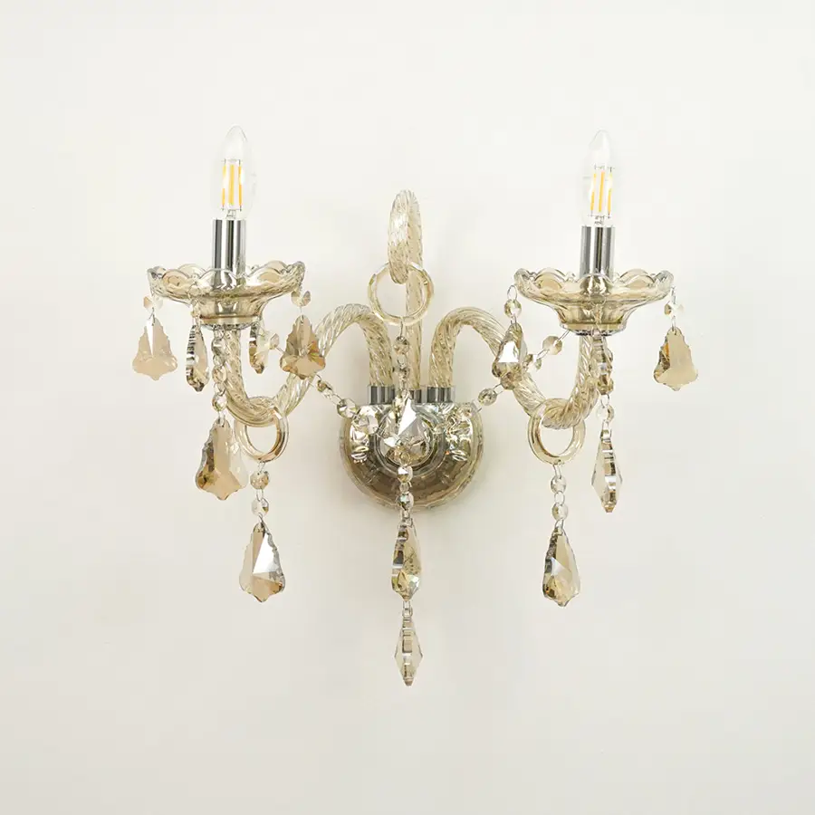 A double-arm wall sconce with a distressed silver metal finish, featuring clear glass candle-style bulbs and hanging faceted crystal drops against a plain white background.