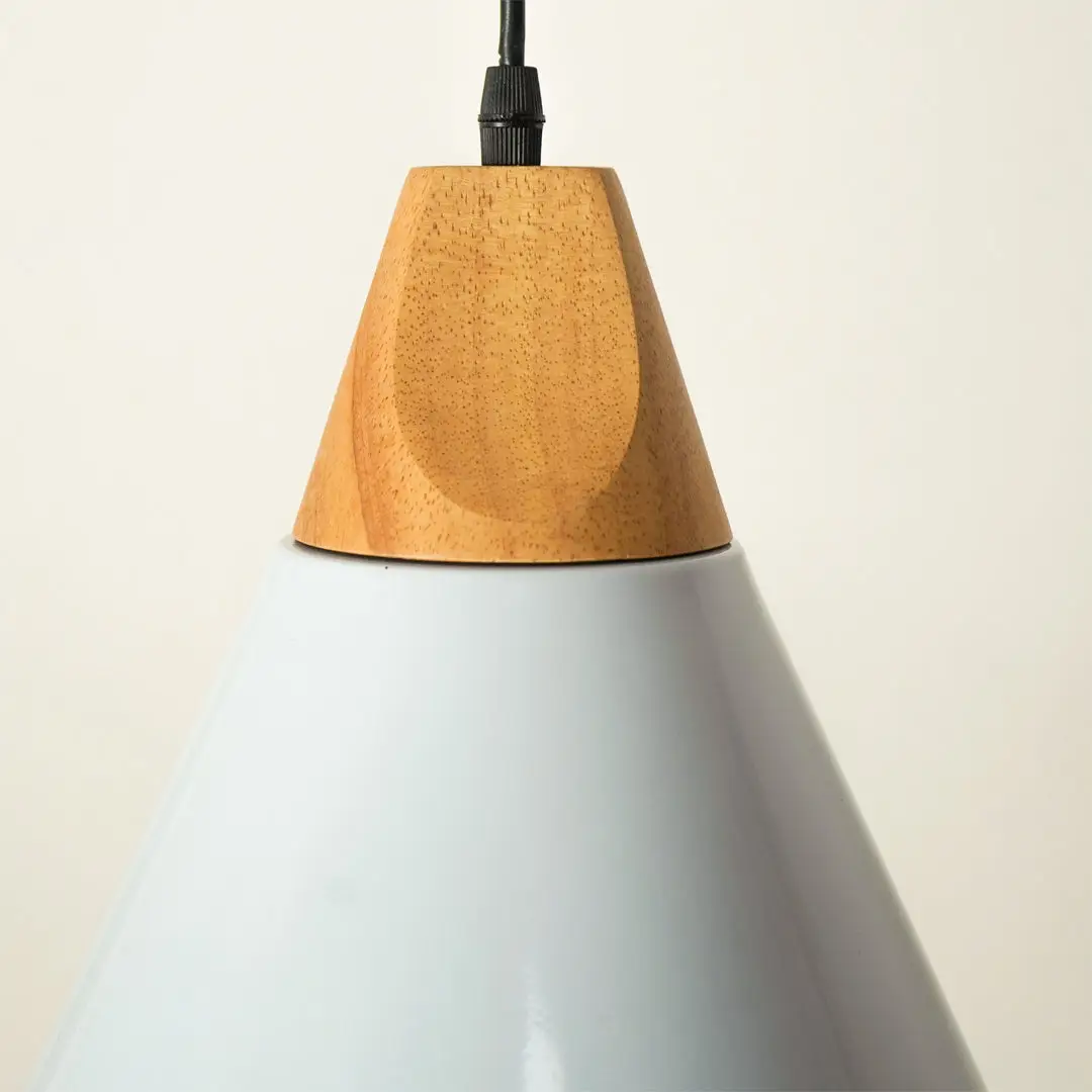 Close-up of a pendant light with a pale blue-gray cone-shaped shade and a natural wood accent ring near the top, suspended by a black cord against a warm off-white background.