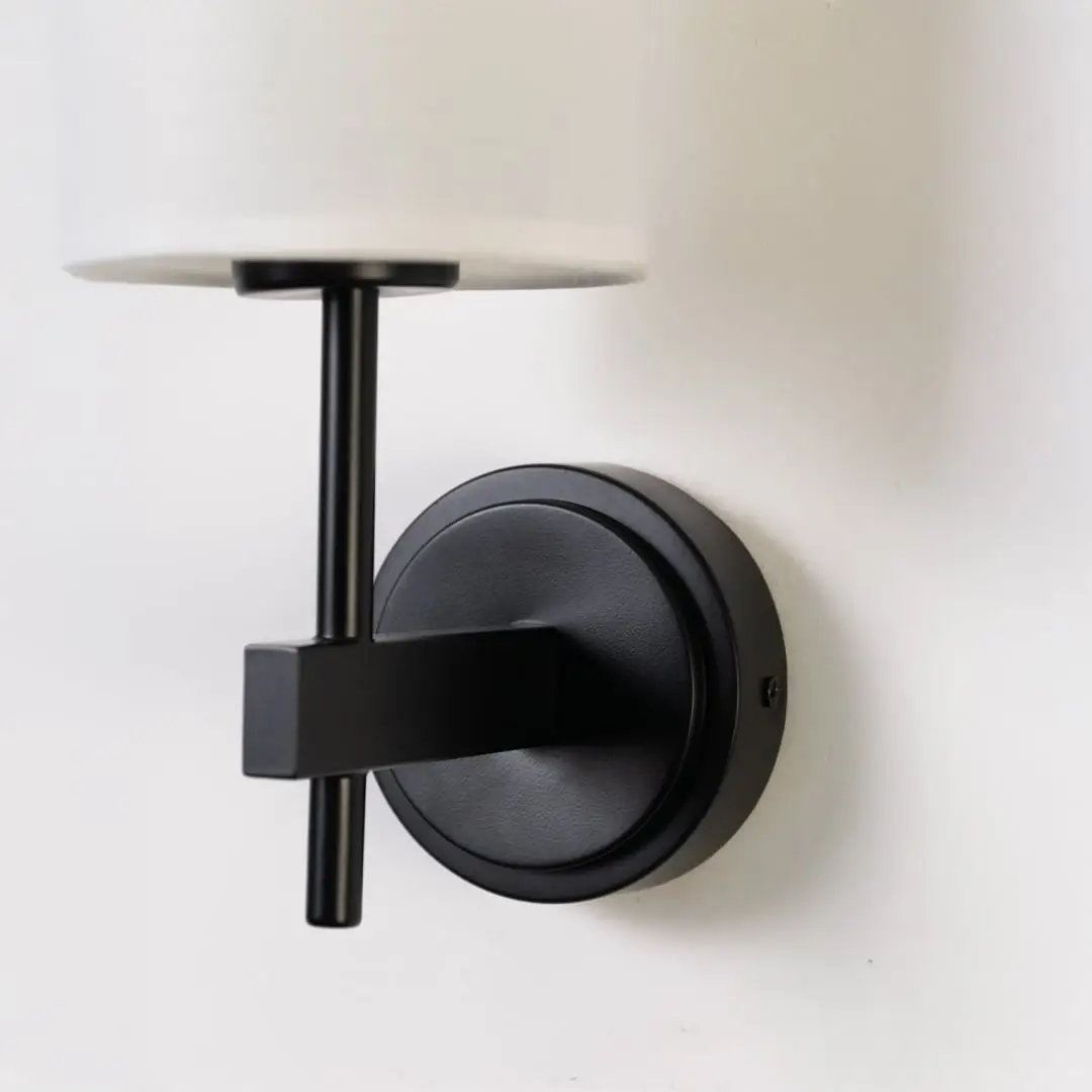 Closeup of black metal wall light with tall white fabric shade showing premium detailing for modern indoor lighting in stylish home interiors.